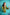 Woman in a green robe holding a bottle against a teal tiled wall. TR